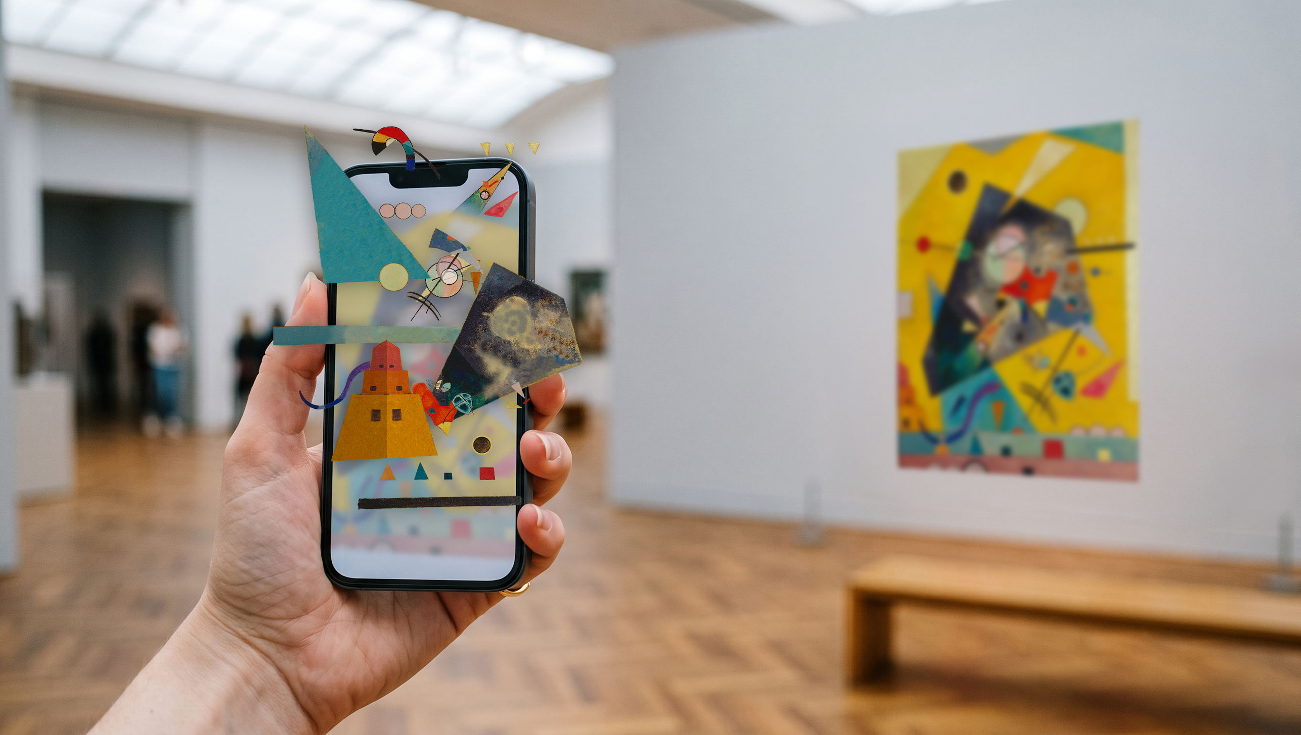 Museum Kunstpalast: eine Hand h&auml;lt ein Smartphone in einen Ausstellungsraum. Auf dem Display setzen sich Formen und Farbfl&auml;chen eines Gem&auml;ldes neu zusammen, einzelne Elemente treten &uuml;ber den Displayrand hinaus in den Raum. Rechts an der Wand h&auml;ngt ein farbiges, abstraktes Gem&auml;lde.