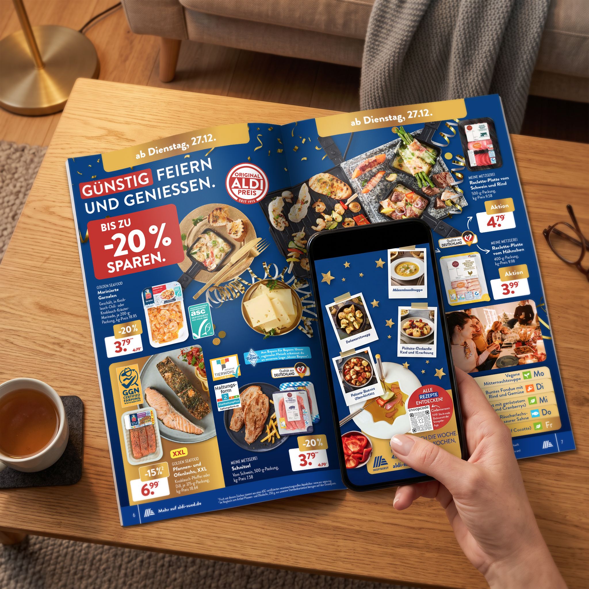 Aufgeschlagener ALDI S&Uuml;D Handzettel auf einem Holztisch im Wohnzimmer, eine Hand h&auml;lt ein Smartphone dar&uuml;ber, auf dem Display springen Rezeptfotos aus der Seite